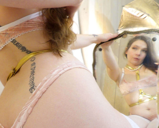 woman admiring gold harness lingerie in mirror