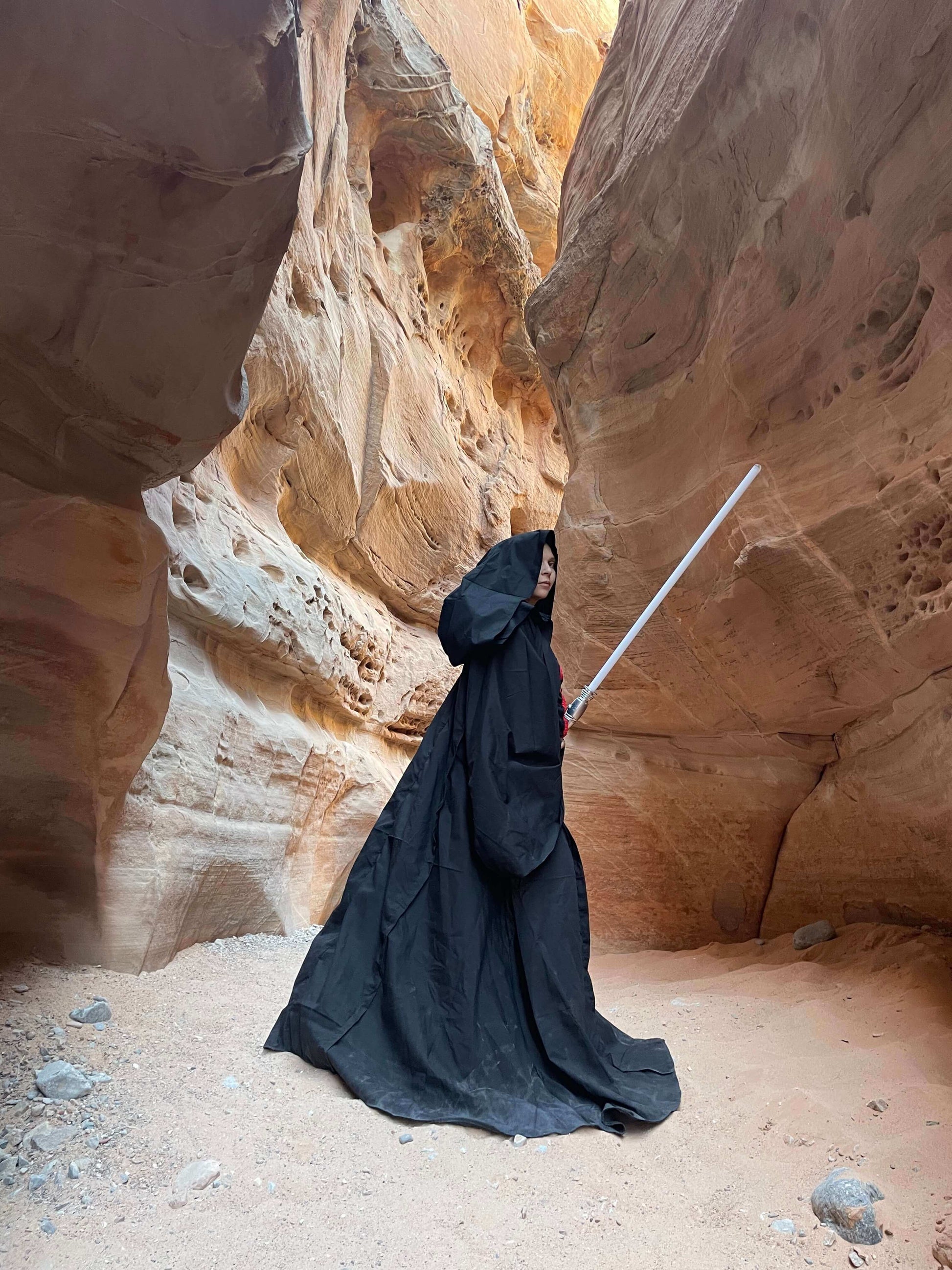 sith cosplayer holding light saber looking over shoulder in desert
