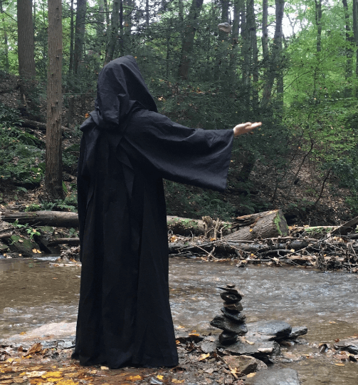 ghostly figure with stones stacked by the river