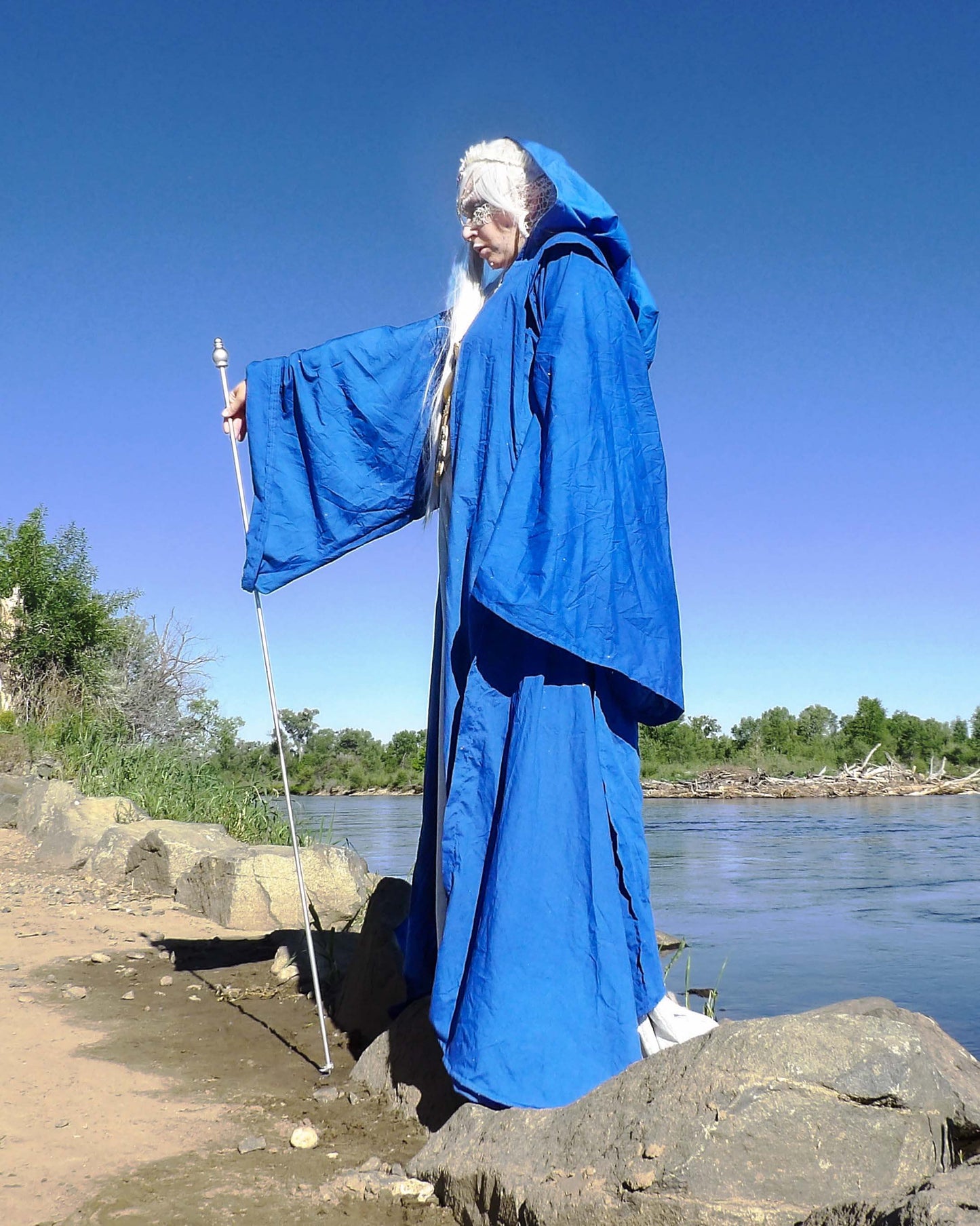 side profile of water elf in blue robe with staff near water edge
